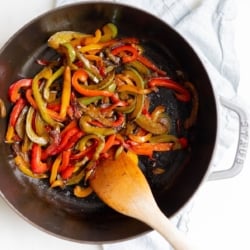 A cast iron pan full of sauteed bell peppers, wooden spoon to the side.