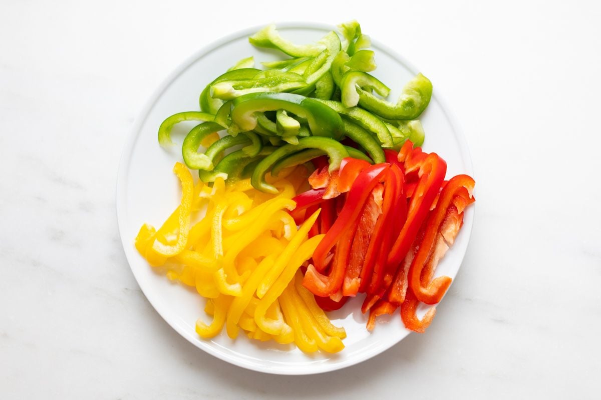 Fresh sliced colorful bell peppers on a white plate, resting on a marble countertop.