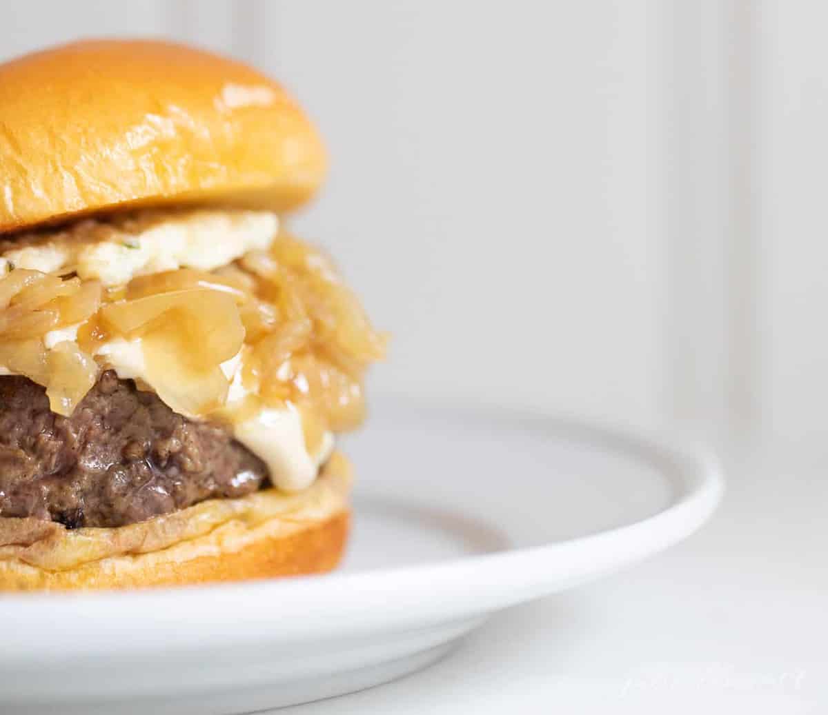 A gourmet burger on a white plate with a white background. 