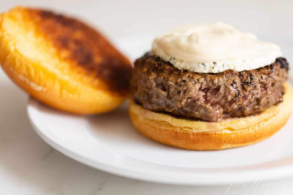 White plate with a burger on a brioche bun, boursin cheese on top.