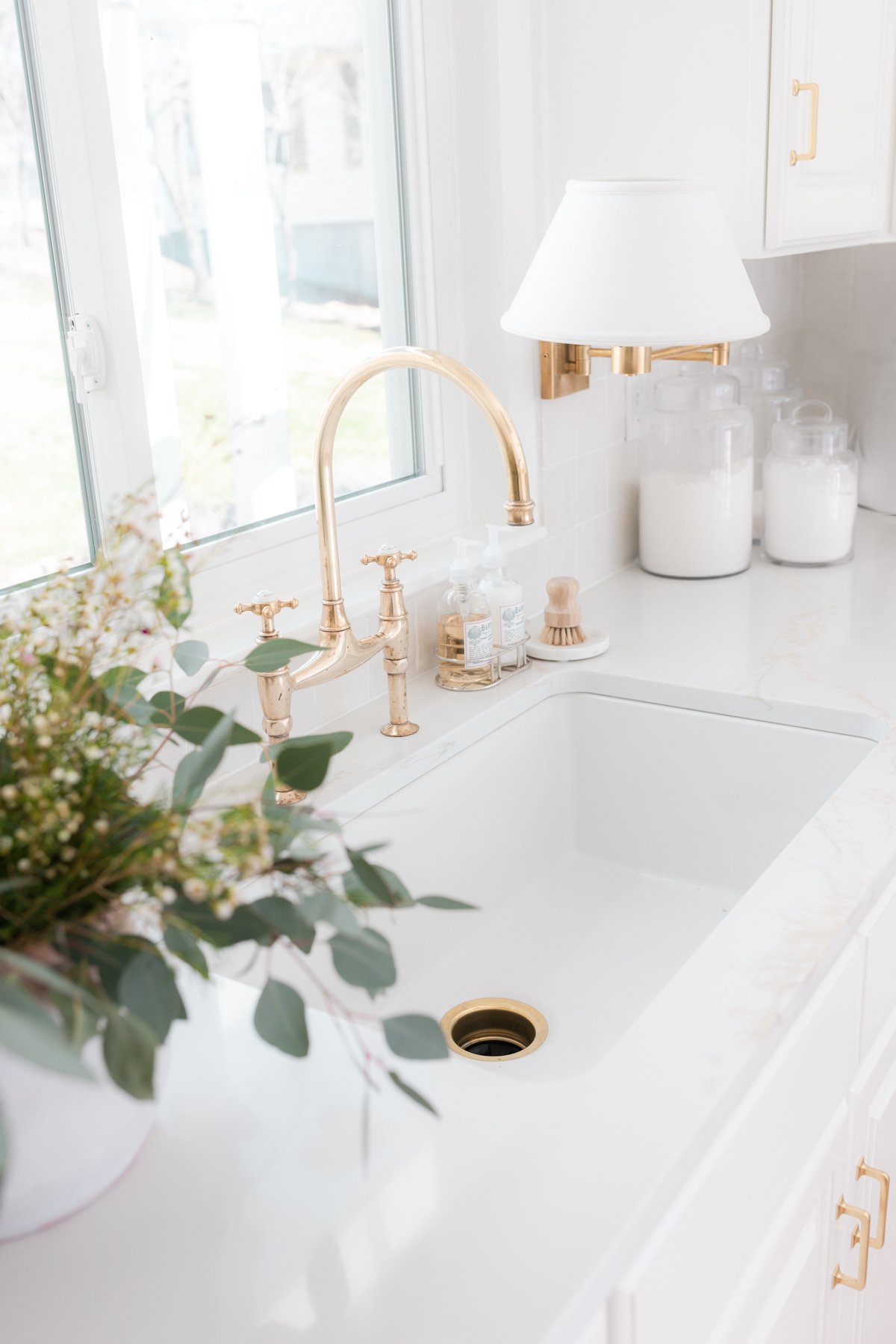 A lkitchen with white finishes and an unlacquered brass kitchen faucet.