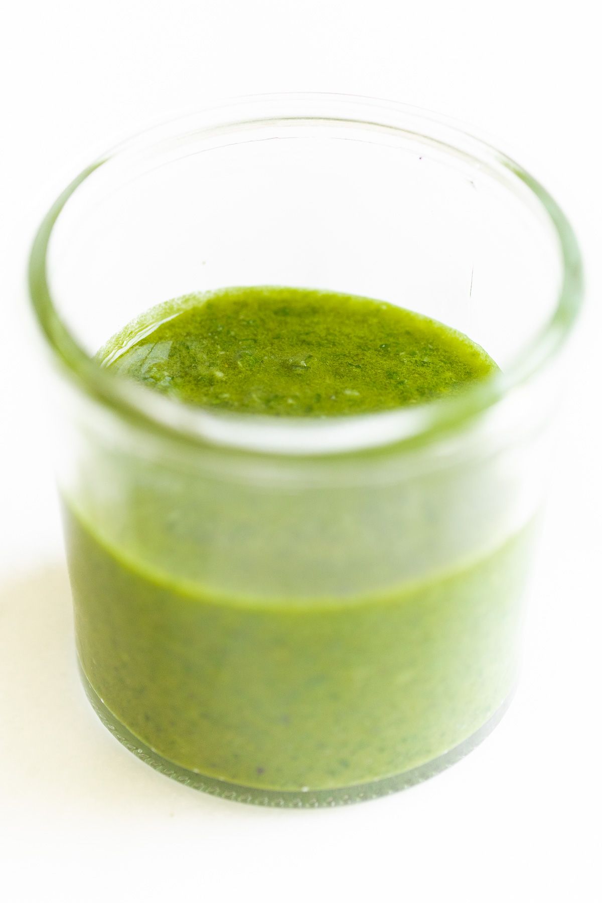 Basil pesto in a small clear glass jar on a marble surface.