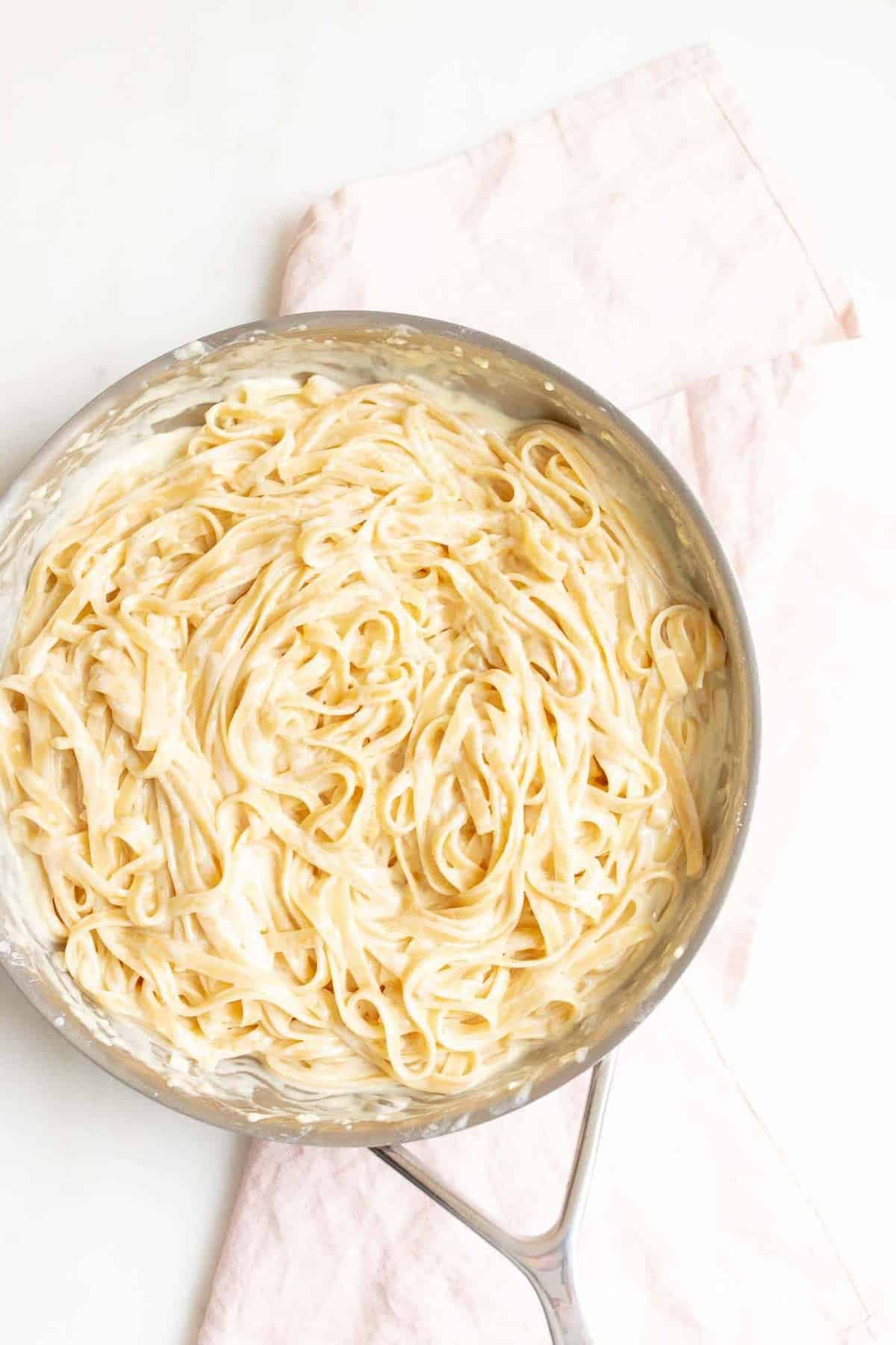 Fettuccine Alfredo in a metal pan on with a pink linen napkin to the side.