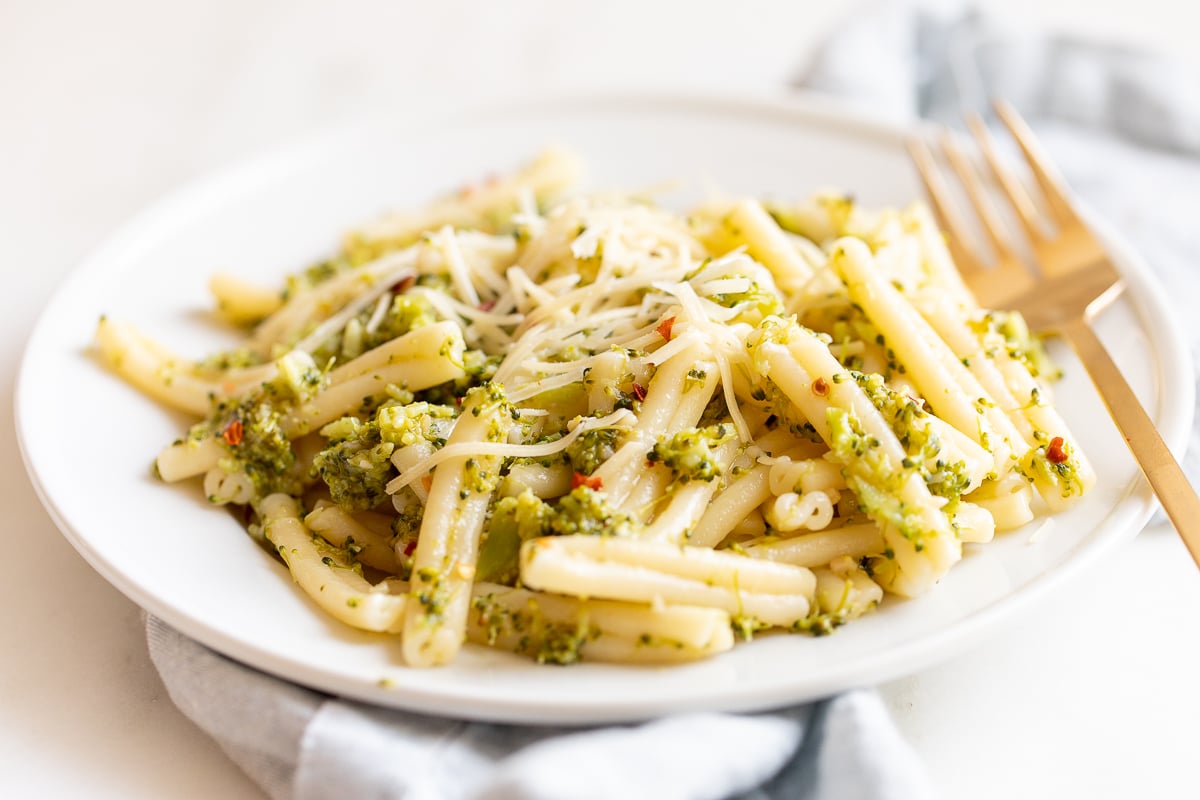 A white plate filled with broccoli pasta, blue napkin behind.