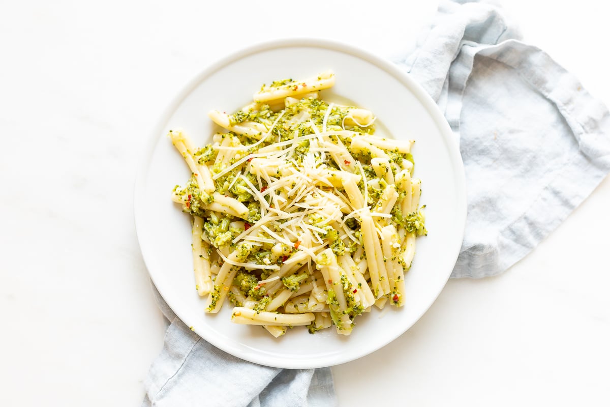 A white plate filled with broccoli pasta, blue napkin behind.