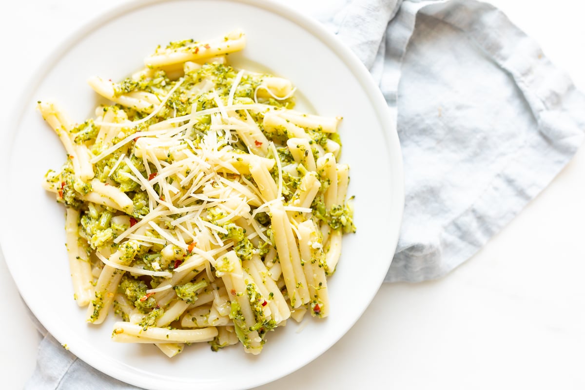 A white plate filled with broccoli pasta, blue napkin behind.