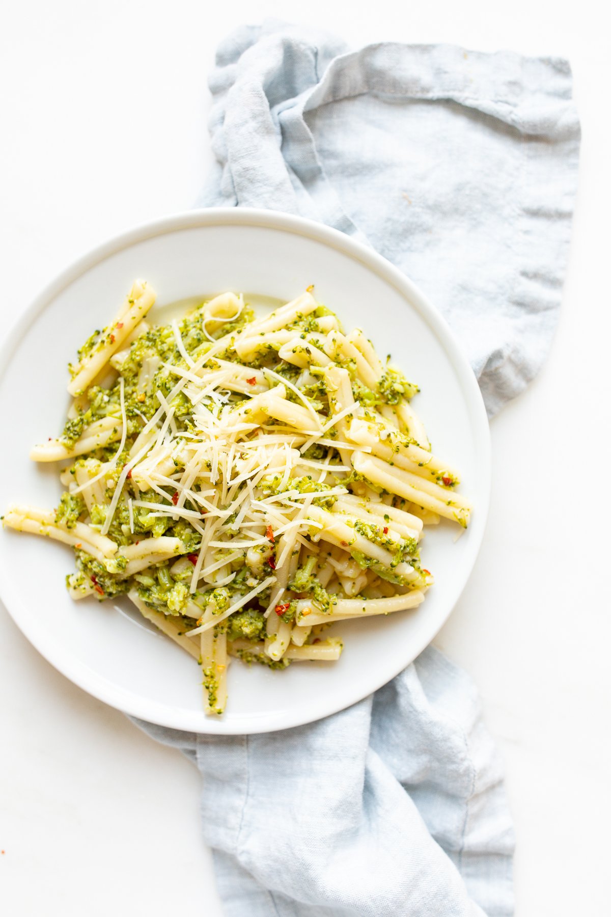 A white plate filled with broccoli pasta, blue napkin behind.