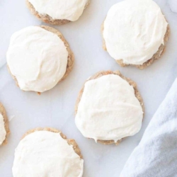 Frosted carrot cake cookies on a marble surface, blue linen towel to the side.