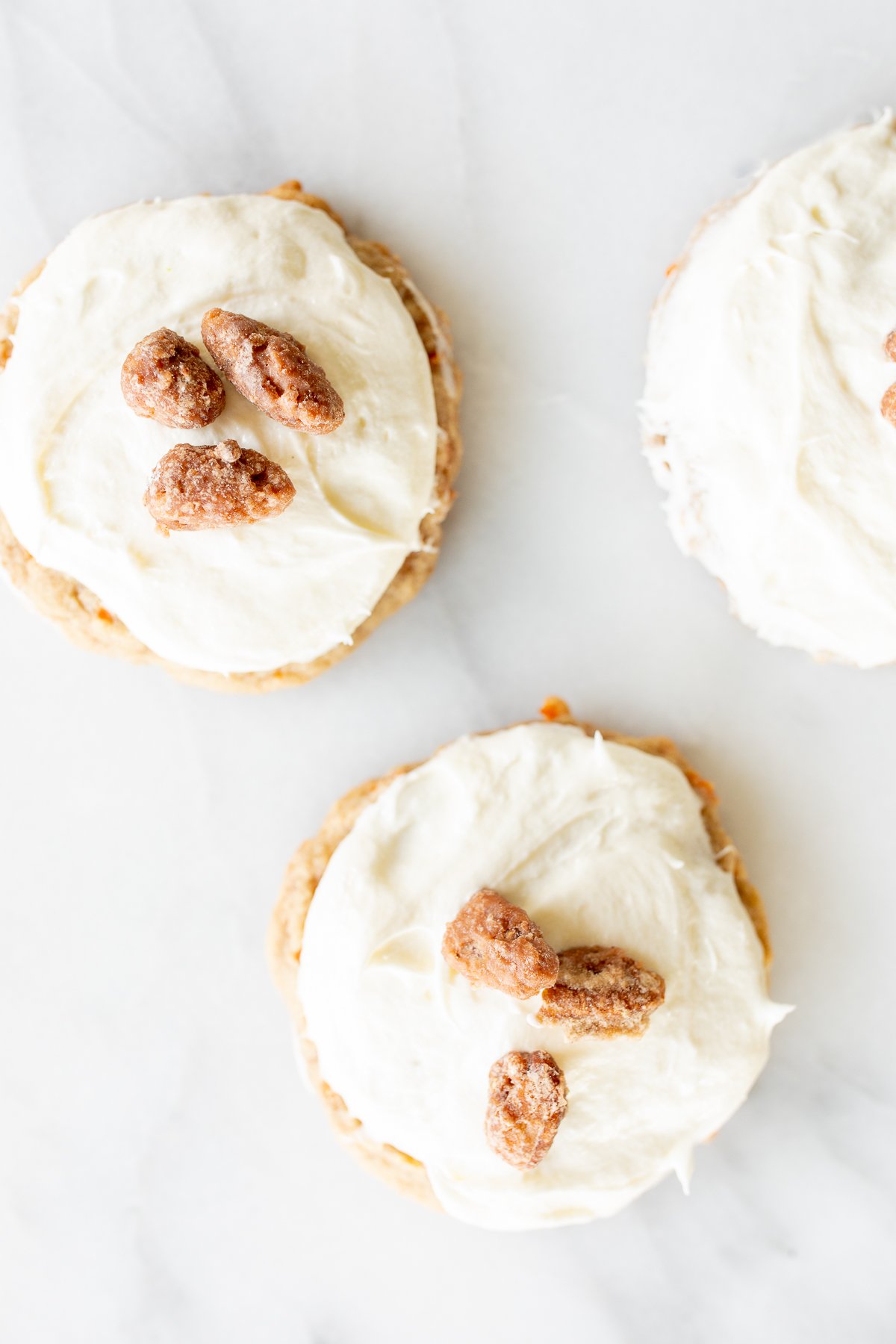 Carrot cake cookies topped with cream cheese frosting and candied pecans on top.