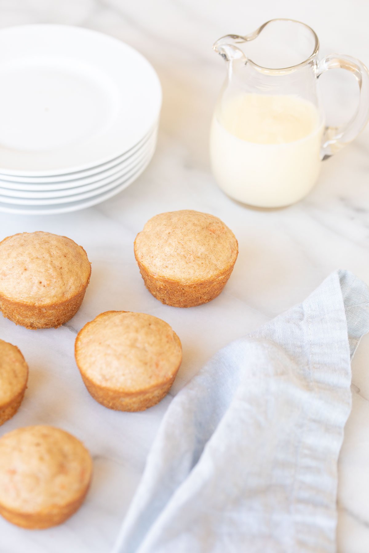 A plate of carrot cake muffins on a table next to a pitcher of milk.