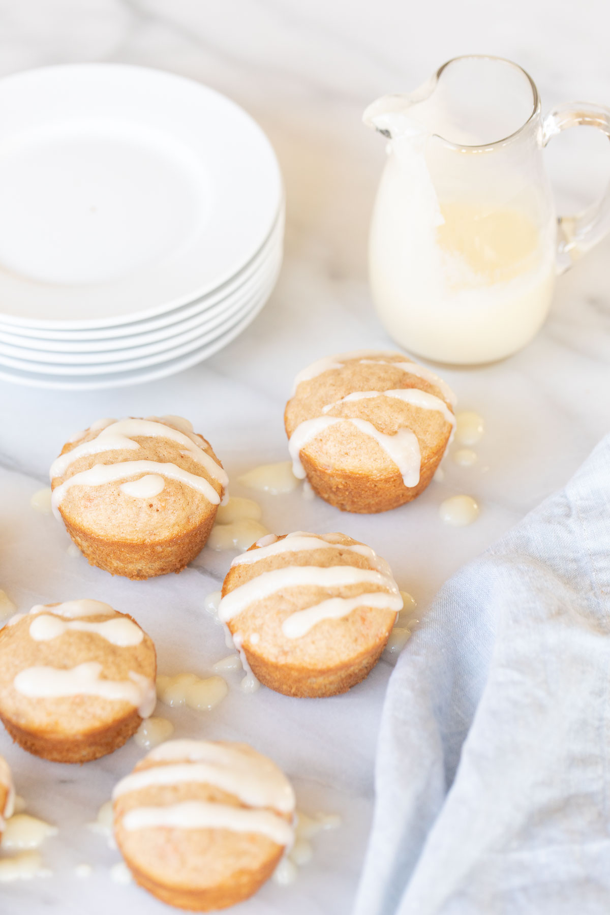 A plate of carrot cake muffins with icing and a pitcher of milk.