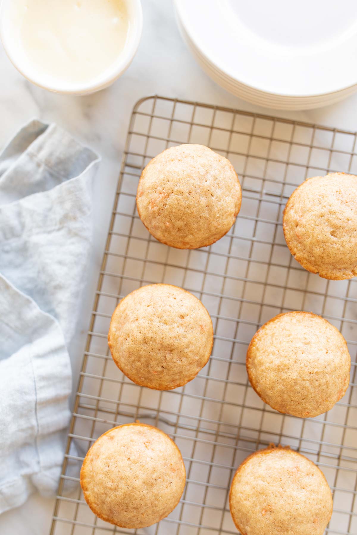 Carrot Cake Muffins on a cooling rack next to a bowl of icing.