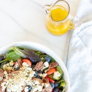 A salad in a white bowl. Champagne vinaigrette in a glass pitcher in the background.