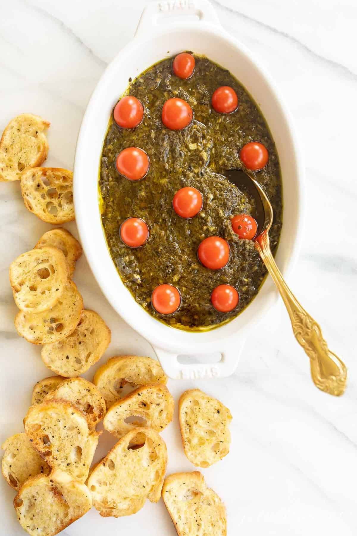 Homemade basil pesto in an oval dish with crostini slices to the side.