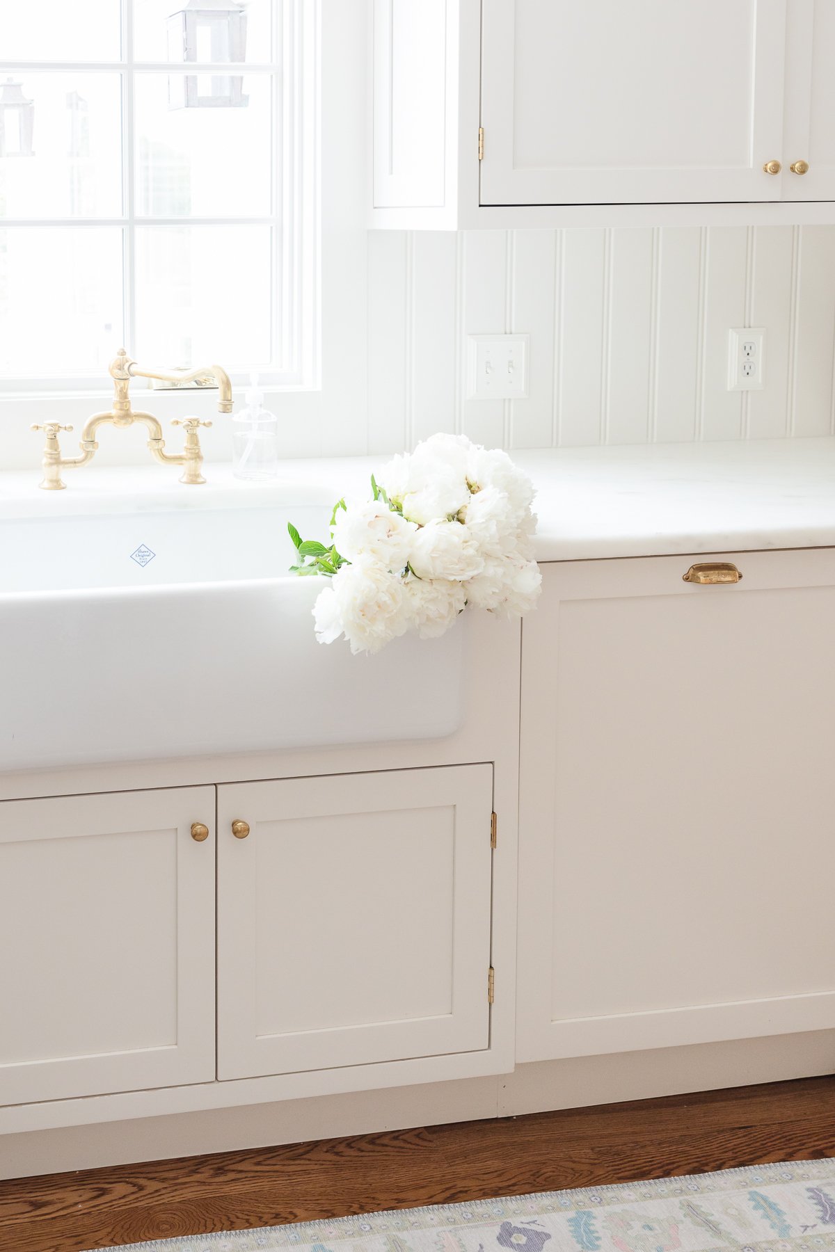 A white kitchen with a farmhouse sink and white flowers.
