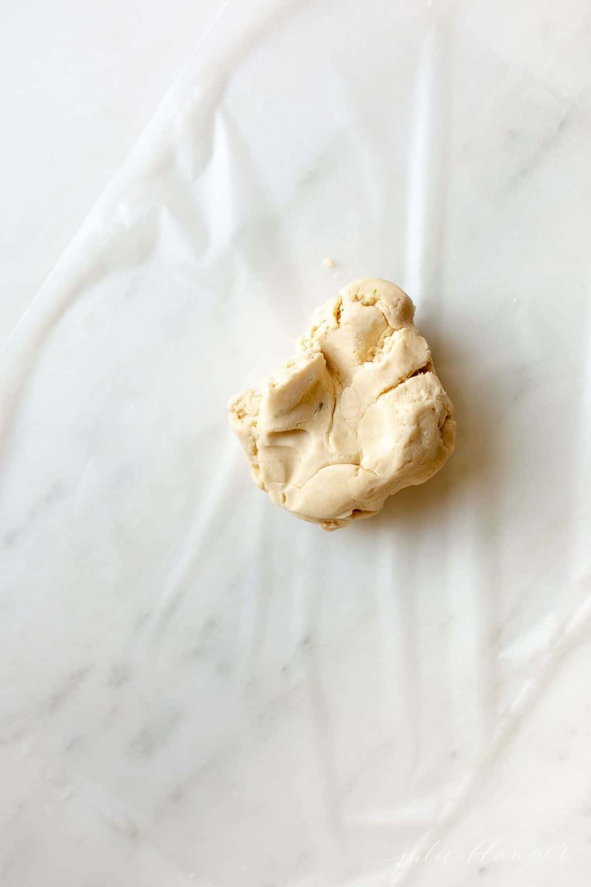 A marble surface with a ball of key lime cookie dough on wax paper.