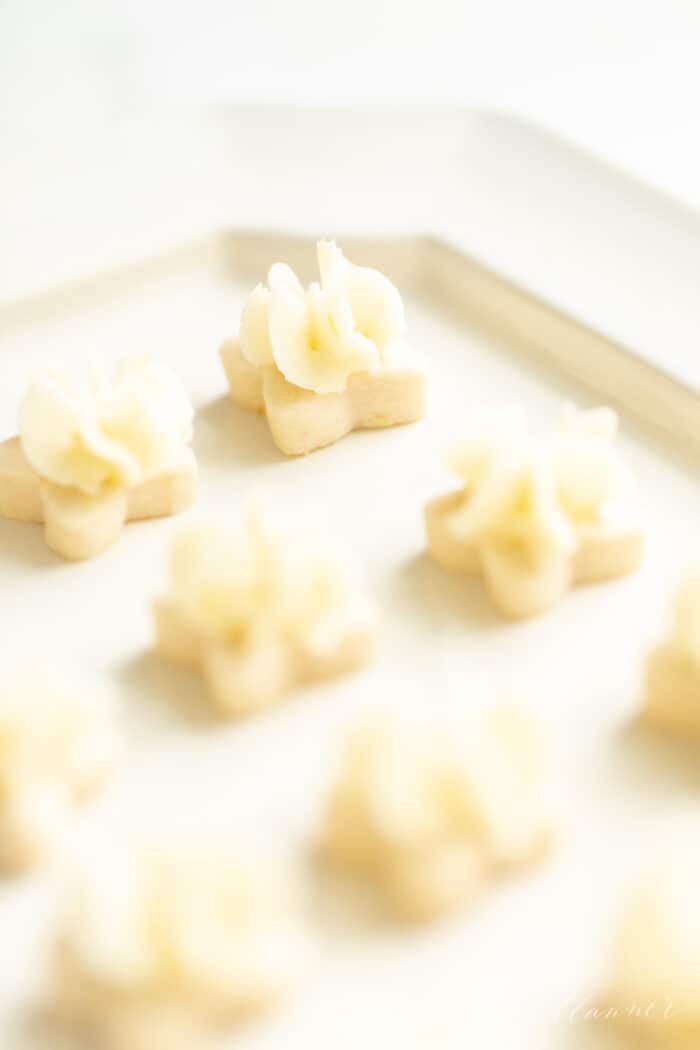 Tiny flower shaped lemon frosted cookies on a white platter.