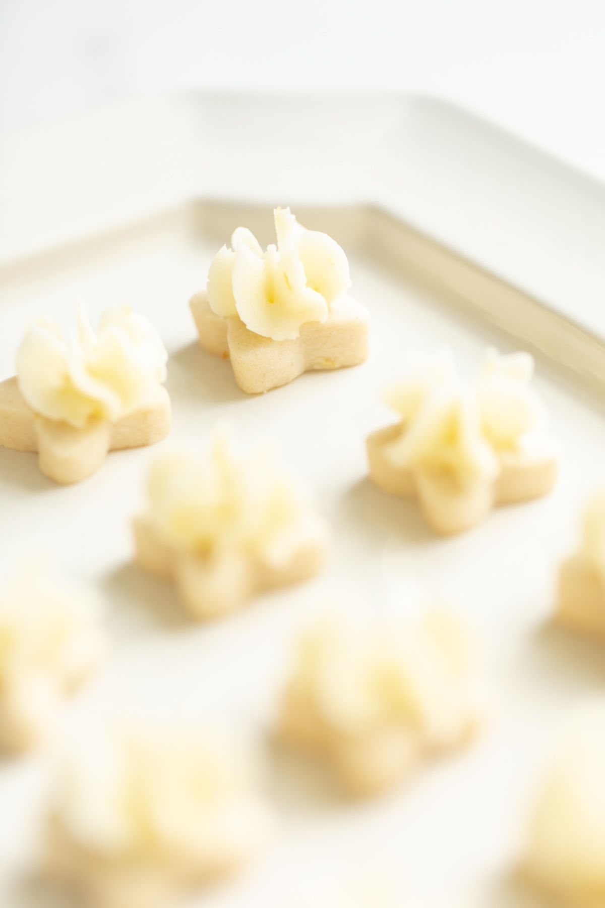 Tiny frosted lemon shortbread cookies on a white platter.