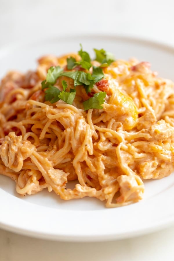 Mexican spaghetti on a white plate, topped with a little cilantro, placed on a white marble countertop.