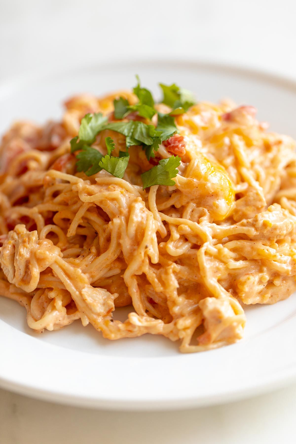 Mexican spaghetti on a white plate, topped with a little cilantro, placed on a white marble countertop.