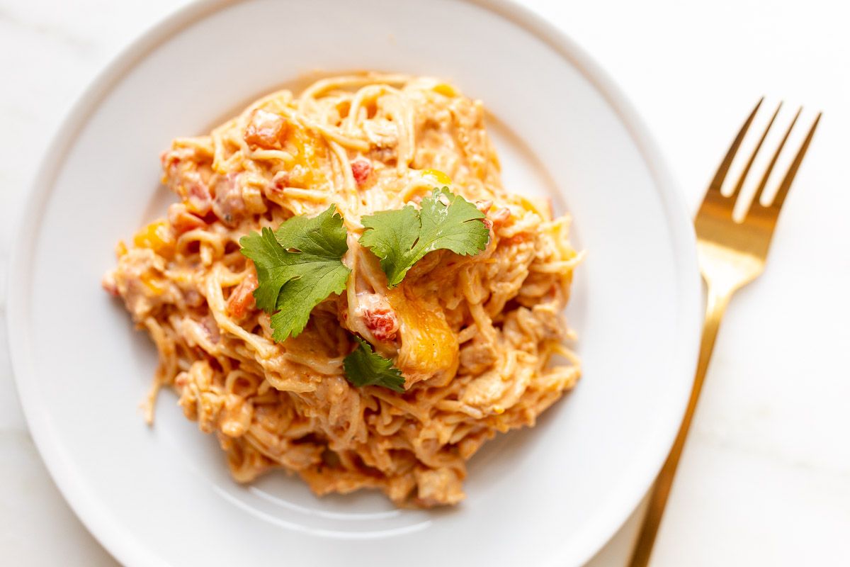 Mexican spaghetti on a white plate, topped with a little cilantro, placed on a white marble countertop.