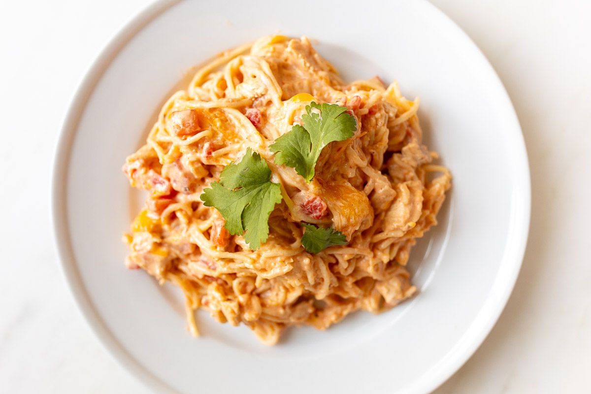 Mexican spaghetti on a white plate, topped with a little cilantro, placed on a white marble countertop.