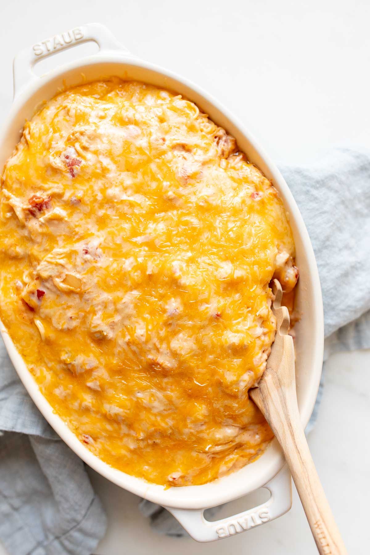 Mexican spaghetti in an oval baking dish, topped with shredded cheese, wooden spoon in the corner.