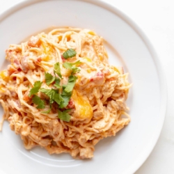 Mexican spaghetti on a white plate, topped with a little cilantro, placed on a white marble countertop.