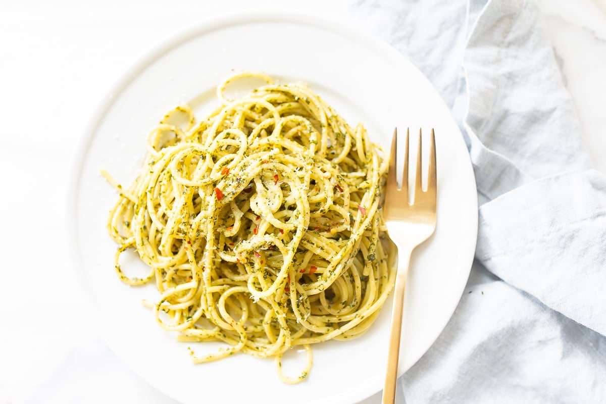 Delicious pesto pasta on a white plate with a fork.