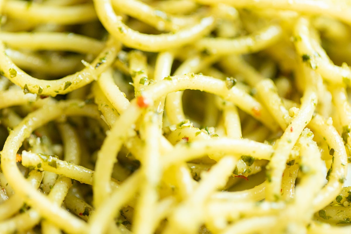 A close up of a bowl of spaghetti with pesto sauce.