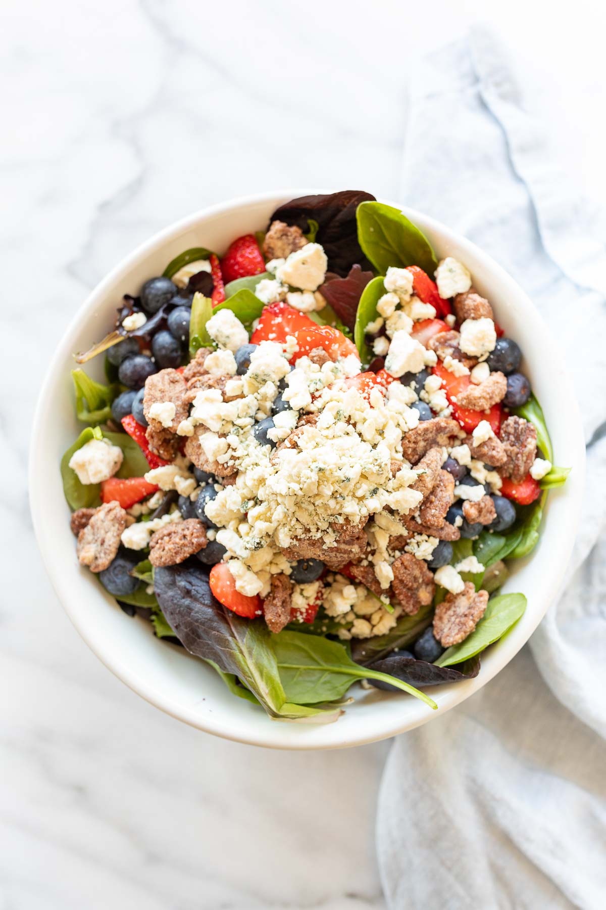 A fresh spring salad with berries, crumbled cheese and nuts in a bowl with wooden serving utensils.