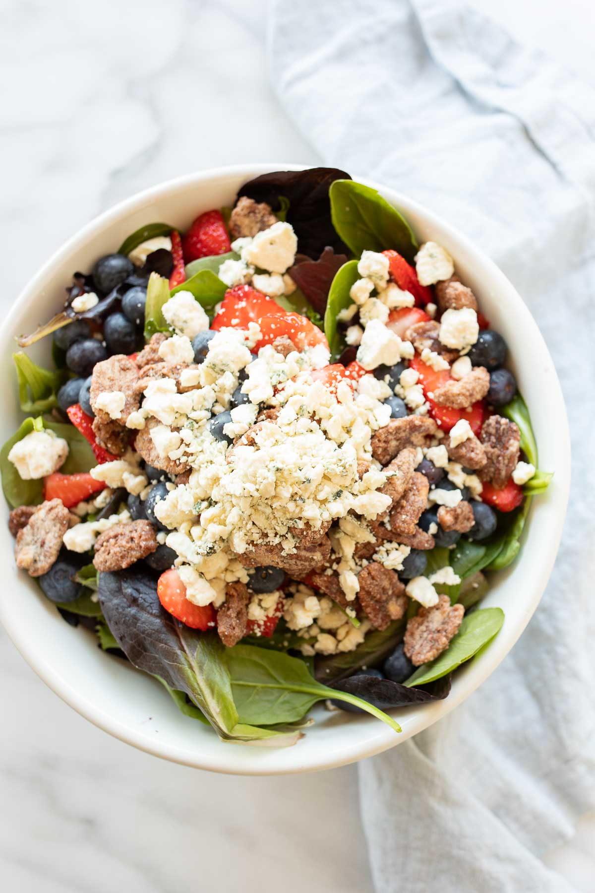 A fresh spring salad with berries, crumbled cheese and nuts in a bowl with wooden serving utensils.