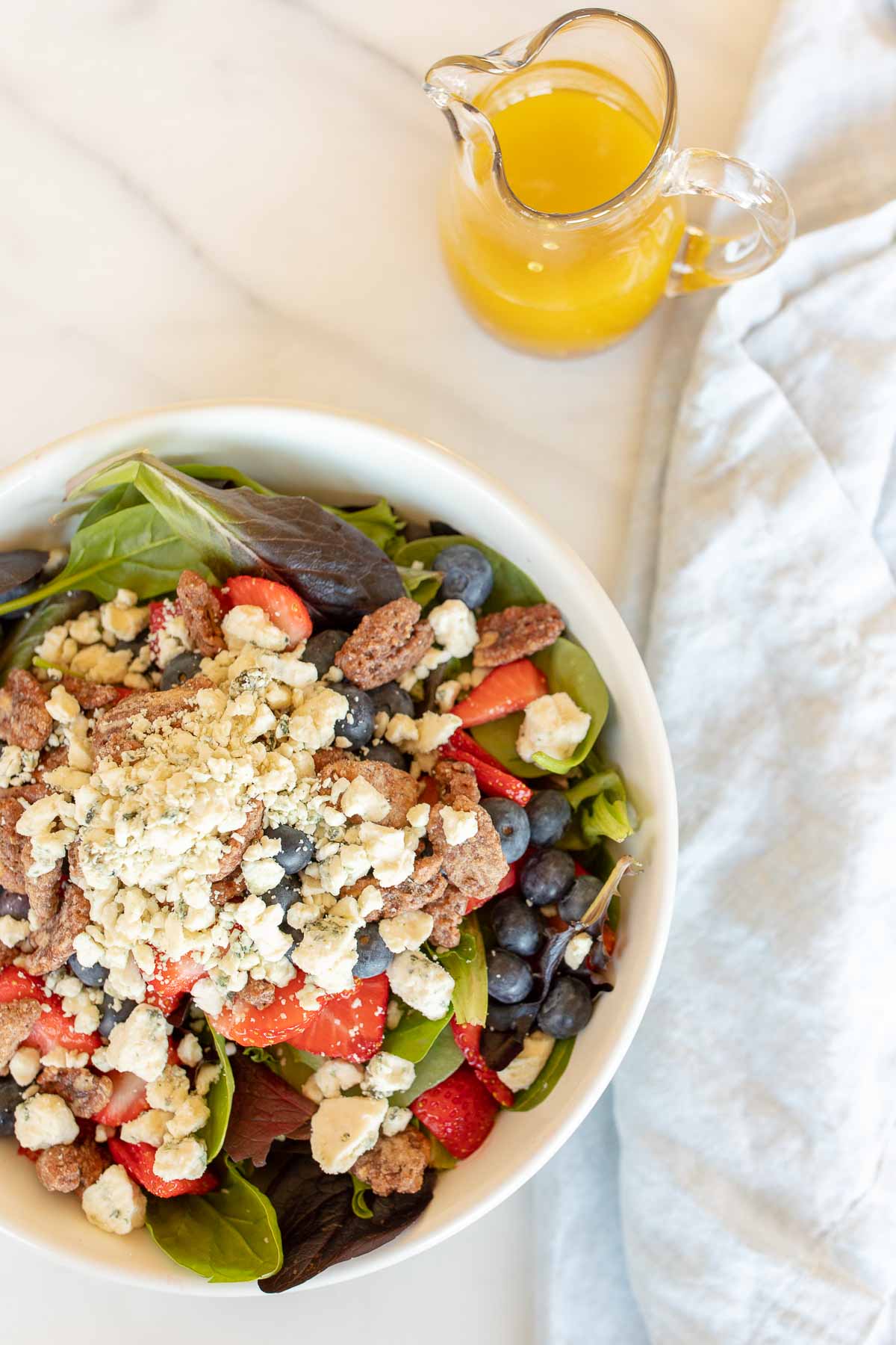 A fresh spring salad with berries, crumbled cheese and nuts in a bowl with wooden serving utensils.