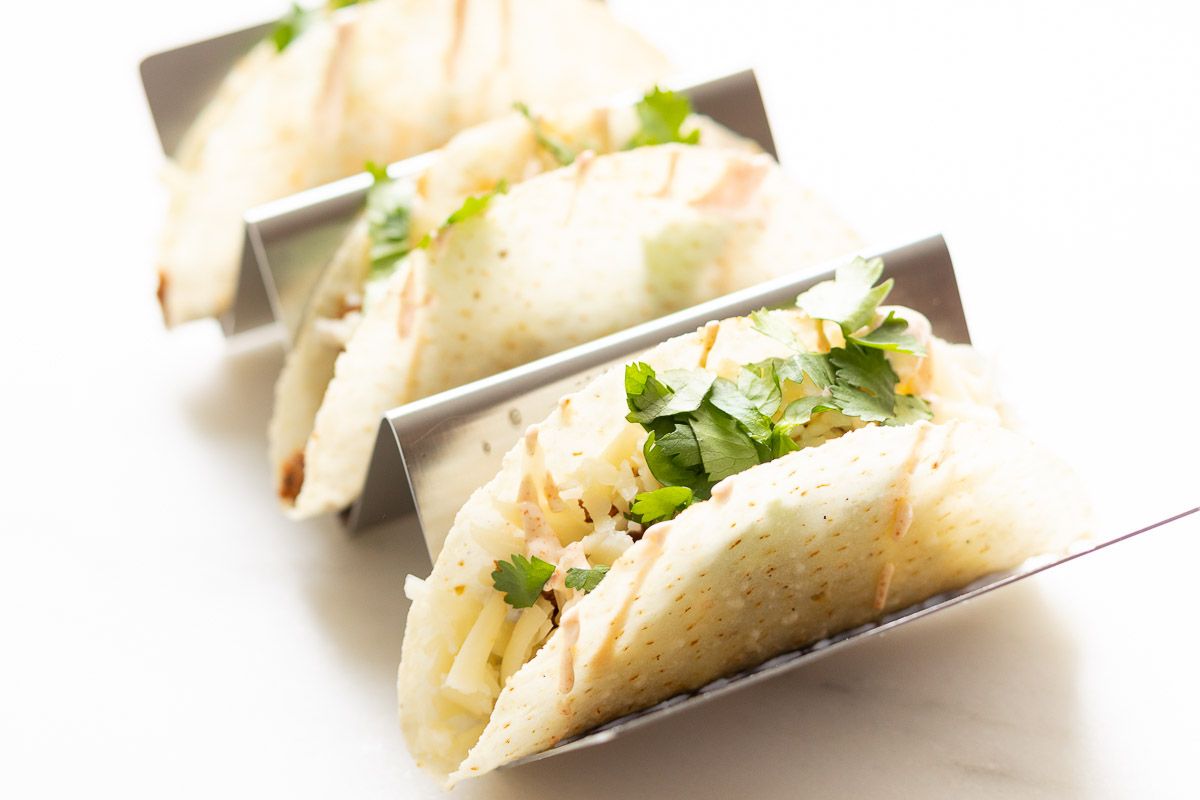 A silver taco holder, holding tacos stuffed with a beef taco meat recipe and topped with cheese and lettuce.