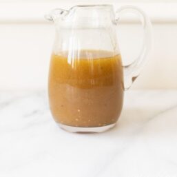 A small glass pitcher filled with a homemade white balsamic dressing, on a marble surface