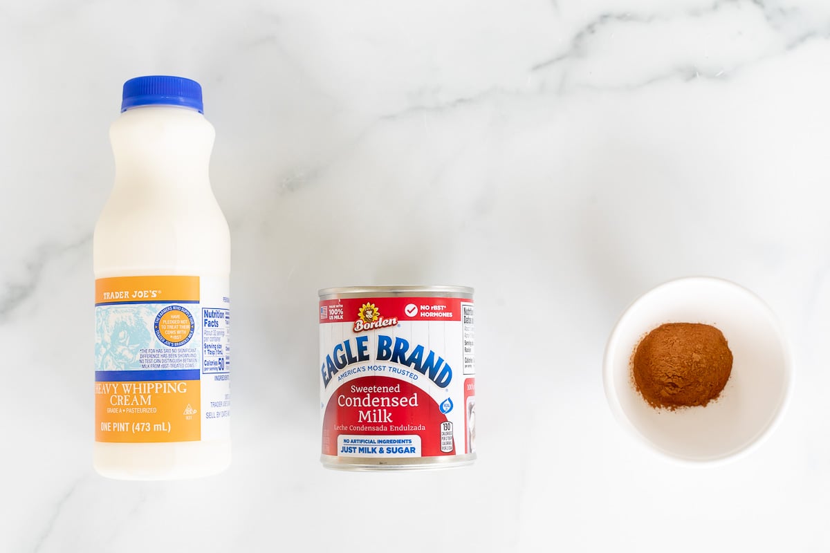 Ingredients for a recipe on a marble surface: a bottle of heavy whipping cream, a can of sweetened condensed milk, and baking substitutions including a bowl of brown sugar.