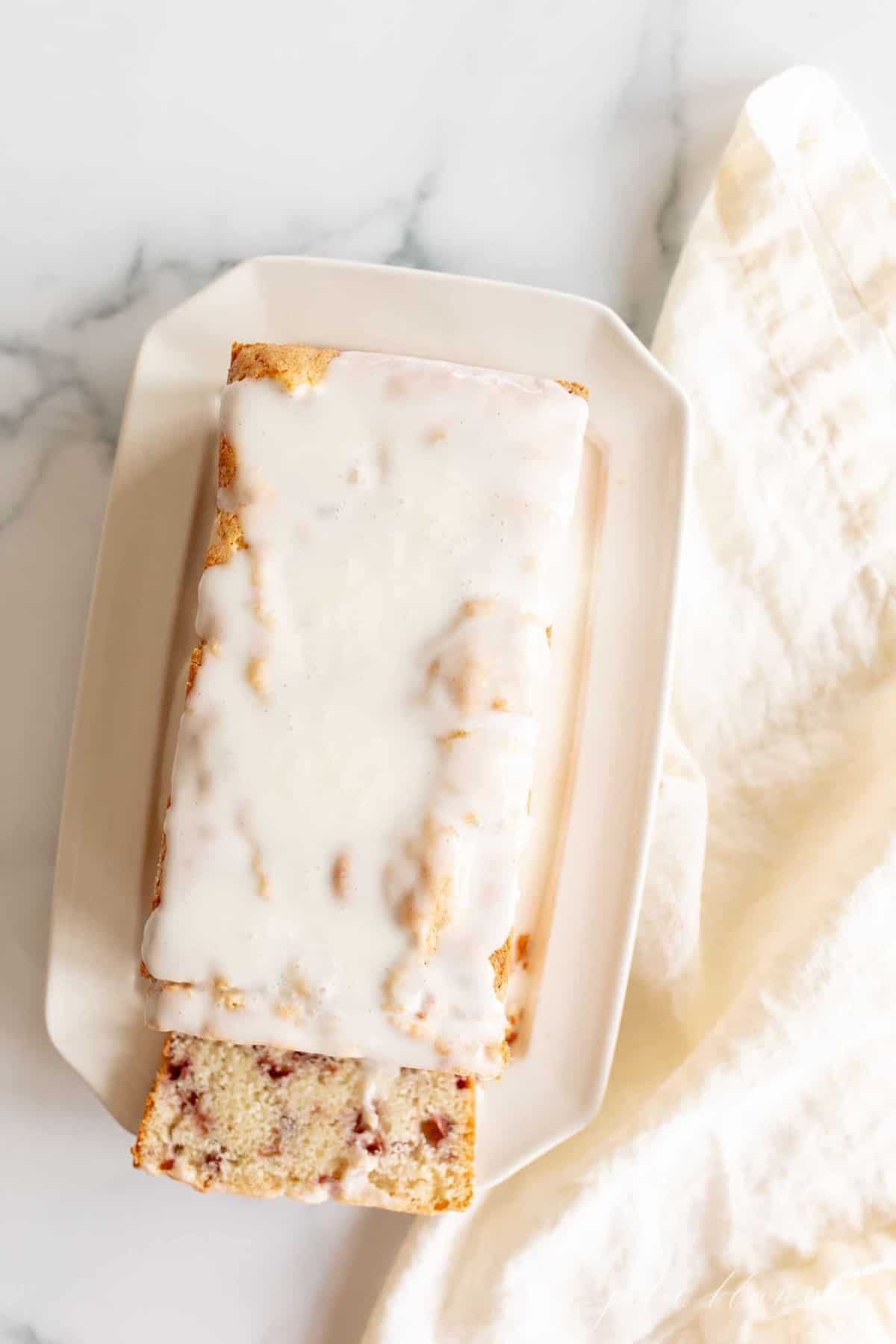 A glazed loaf of strawberry bread recipe on an ivory tray.