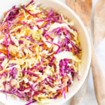 White salad bowl filled with colorful cabbage salad and wooden serving spoons.