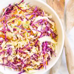 White salad bowl filled with colorful cabbage salad and wooden serving spoons.