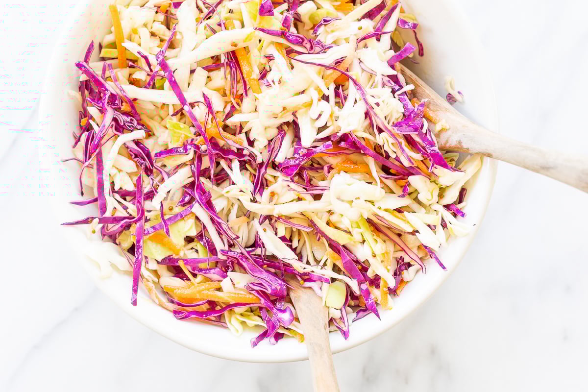 White salad bowl filled with colorful cabbage salad and wooden serving spoons.