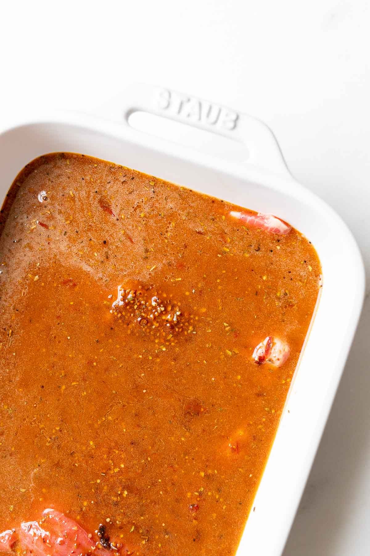 A white baking dish with a steak resting in a carne asada marinade