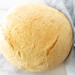 A marble surface with a round loaf of Dutch oven homemade bread, blue linen napkin to the side.