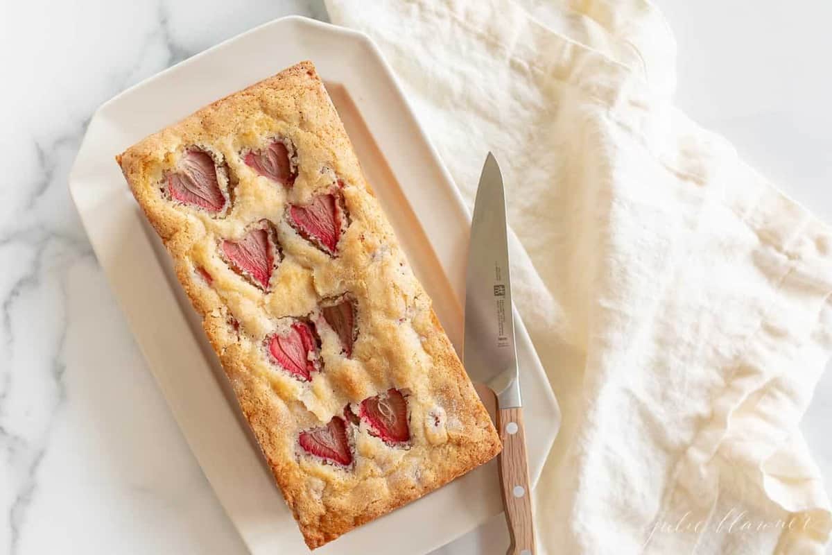 An ivory platter with a fresh loaf of strawberry bread, knife to the side.