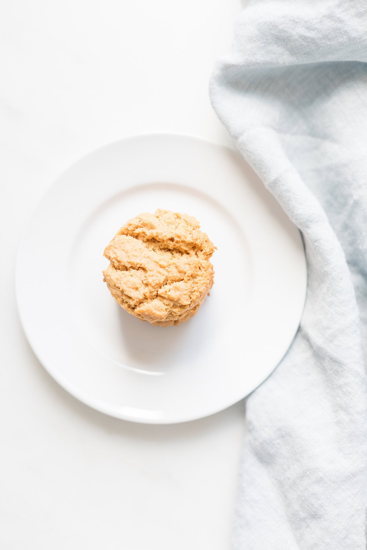 A single scone rests on a white plate beside a light blue cloth, reminiscent of the simplicity found in flourless peanut butter cookies.