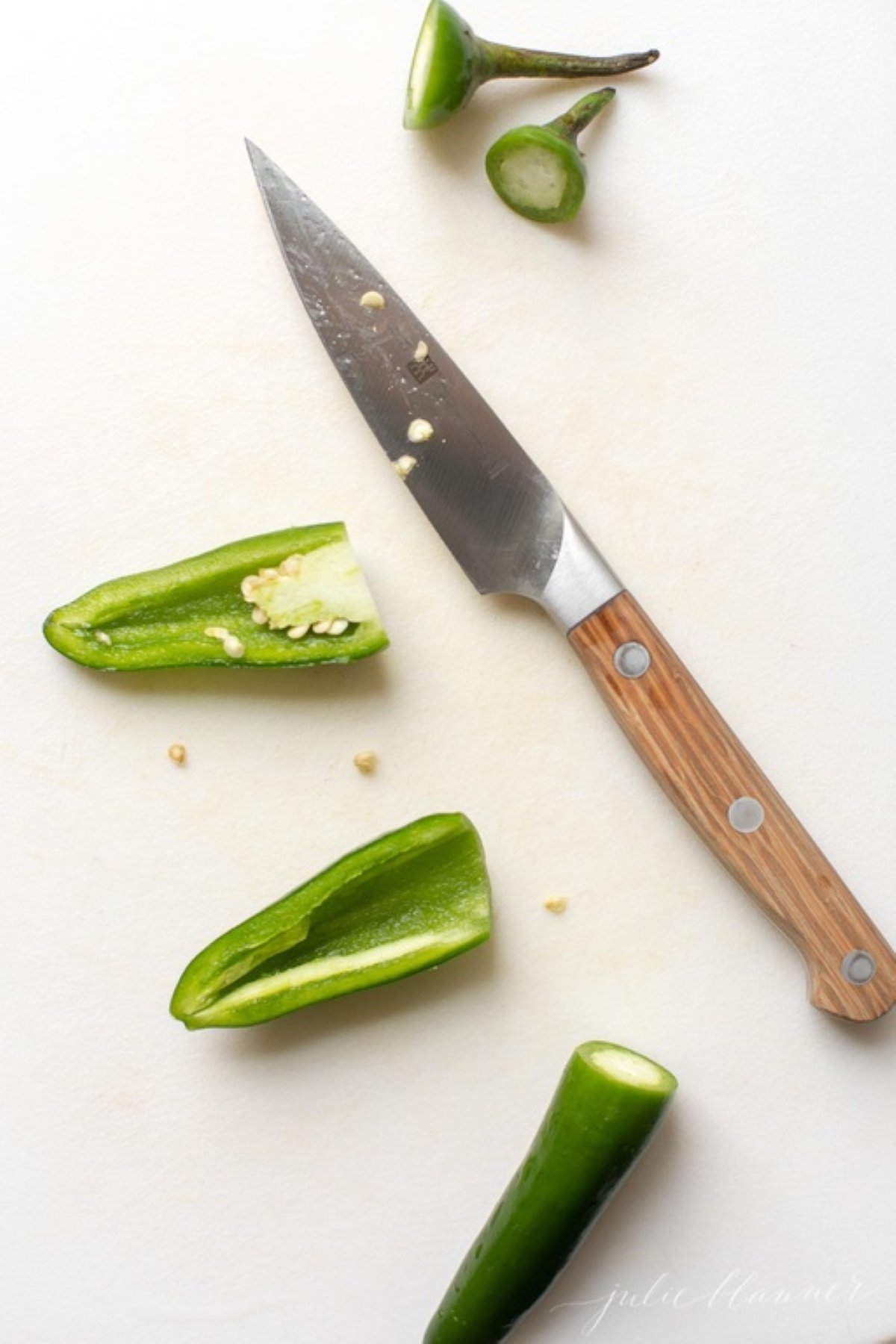 A knife and some cut up jalapenos on a marble countertop.