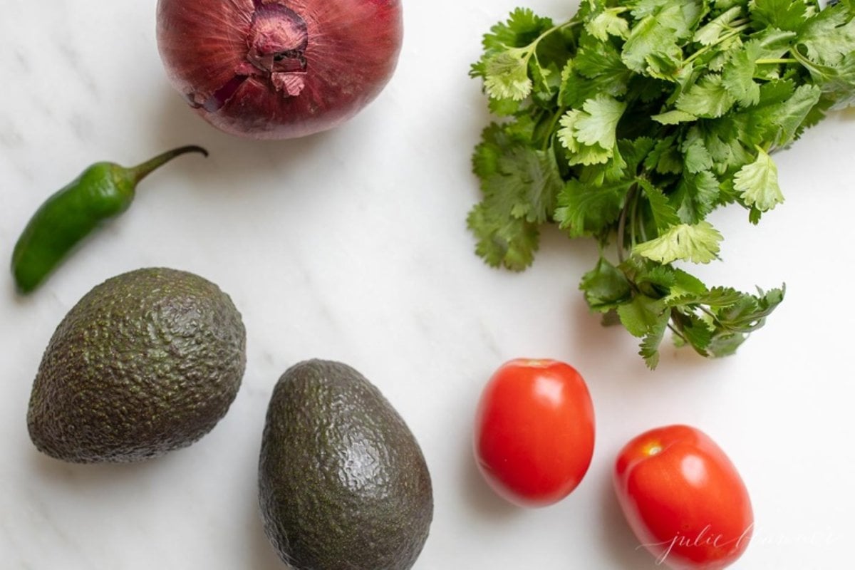 Ingredients for homemade guacamole laid out on a marble countertop.