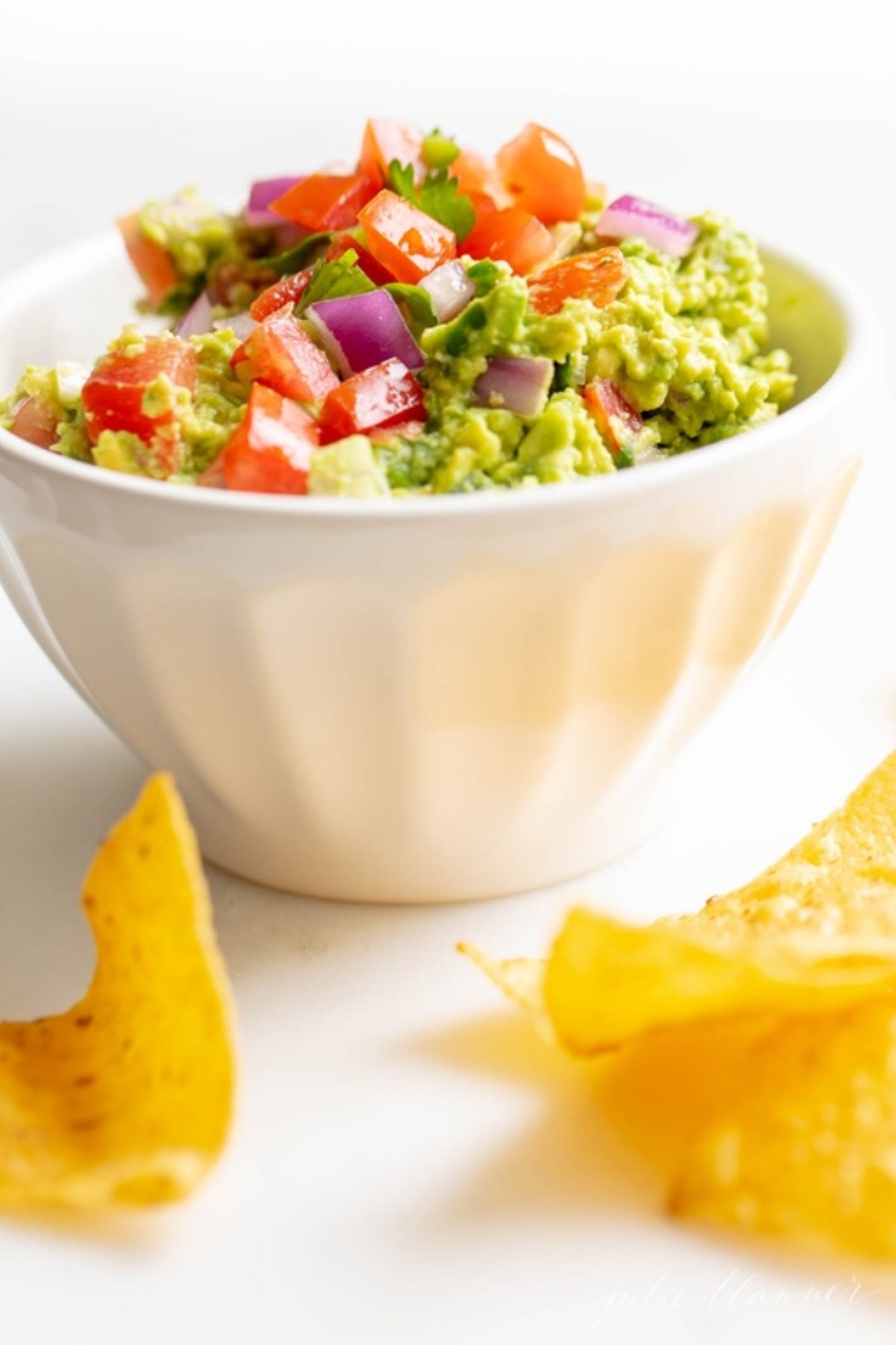 A white bowl full of fresh homemade guacamole., surrounded by tortilla chips.