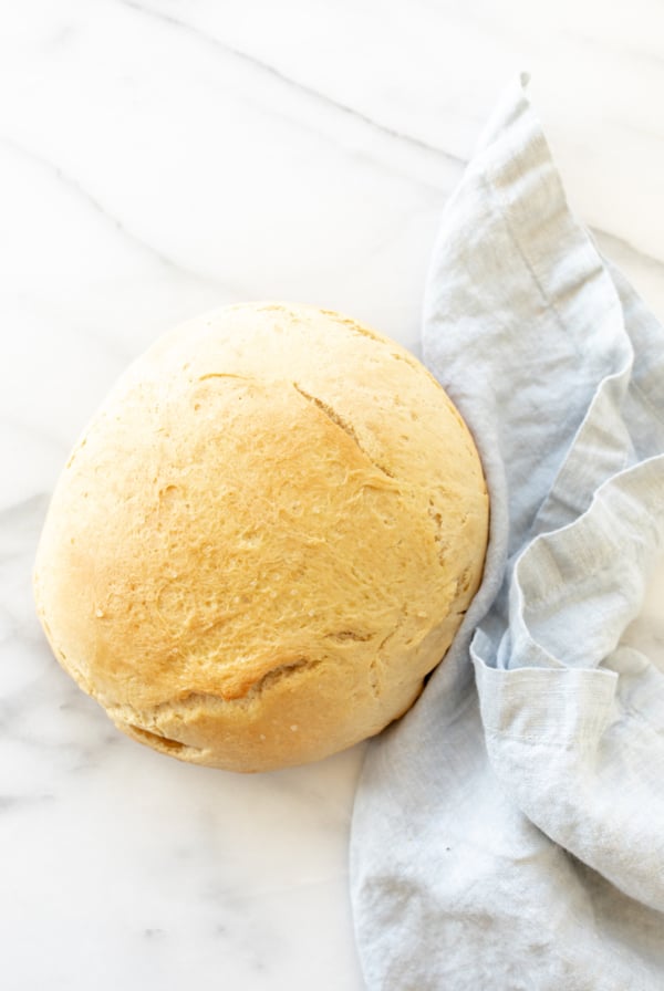 A marble surface with a round loaf of Dutch oven homemade bread, blue linen napkin to the side.