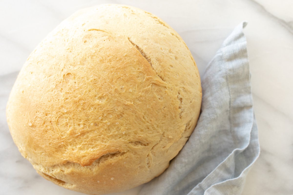 A marble surface with a round loaf of homemade bread, blue linen napkin to the side.