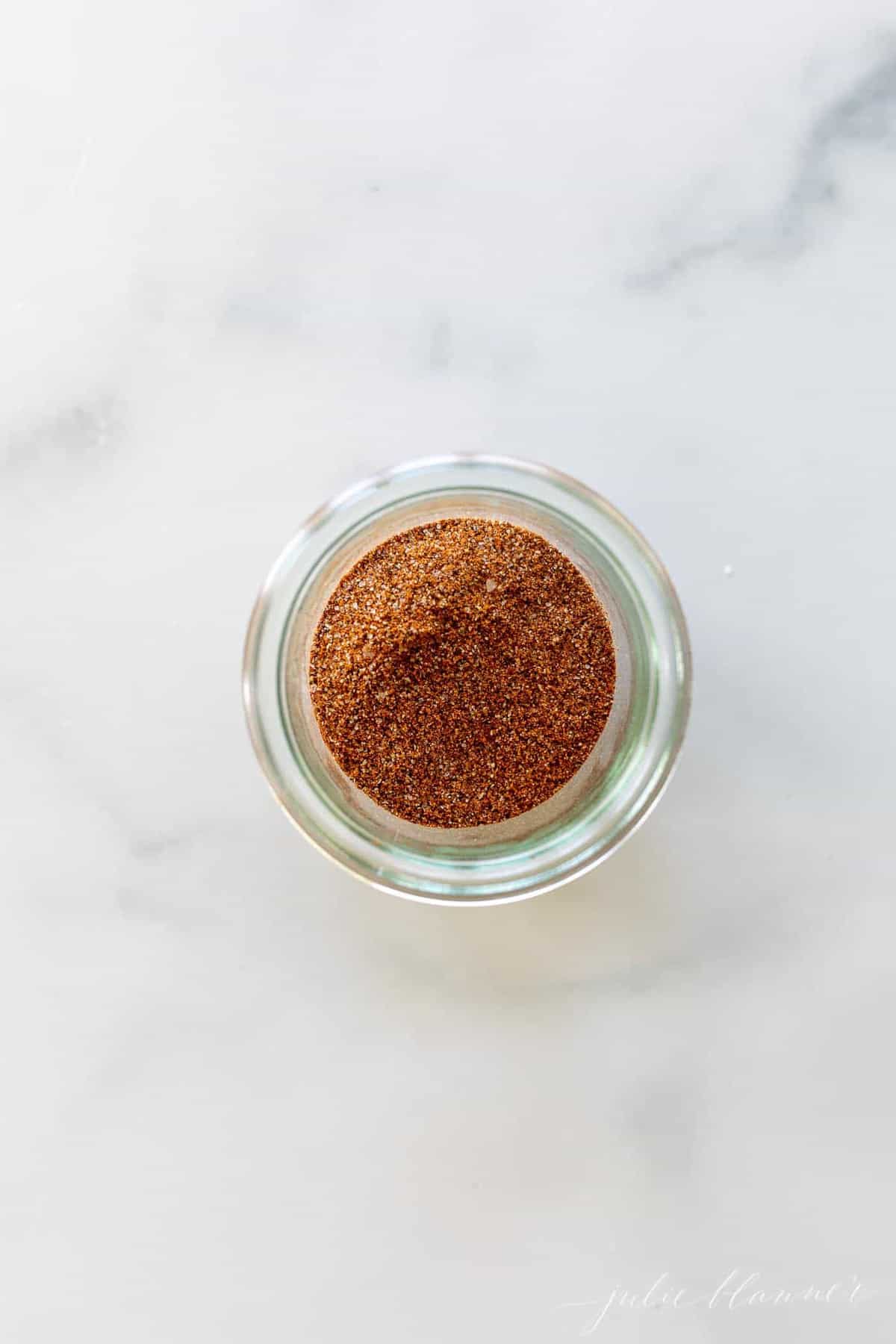 A marble surface with a clear glass jar full of homemade fajita seasoning mix.